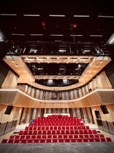The inside of York St John University in the UK. It is in an event space with rows of red chairs and you can see all the way up to the ceiling, where various bits of rigging can be seen.
