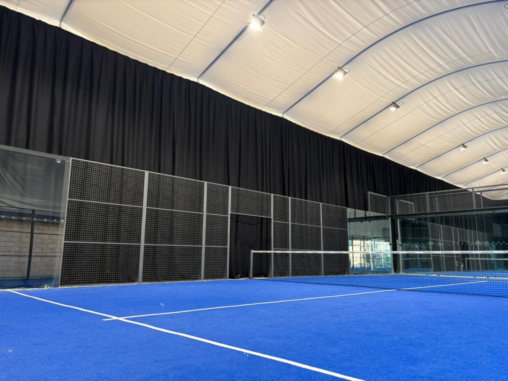 An indoor sports centre with acoustic drapery. This indoor sports centre is showing a tennis/padel court.